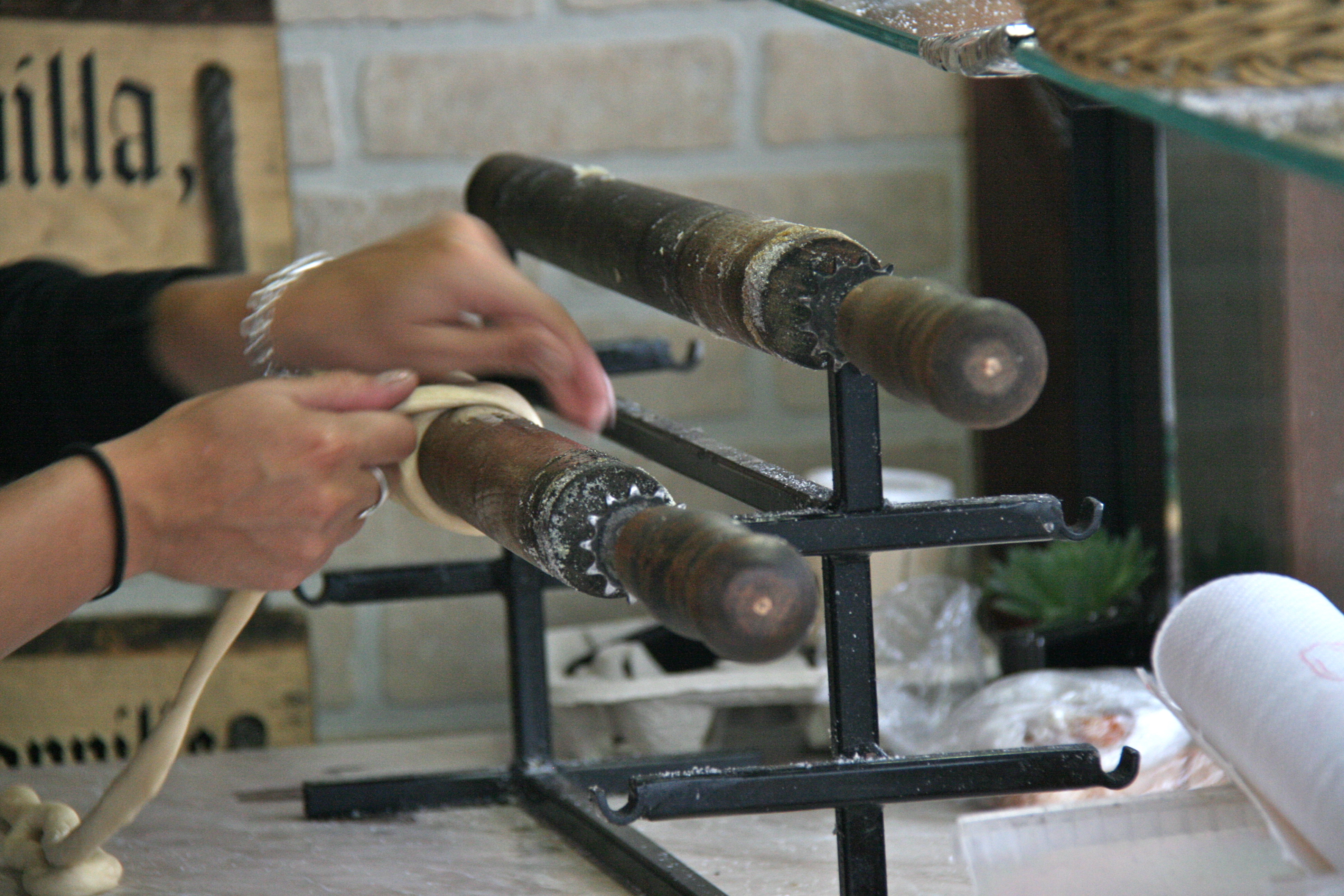 Dough being wrapped around wooden trdlo rollers for trdelnik
