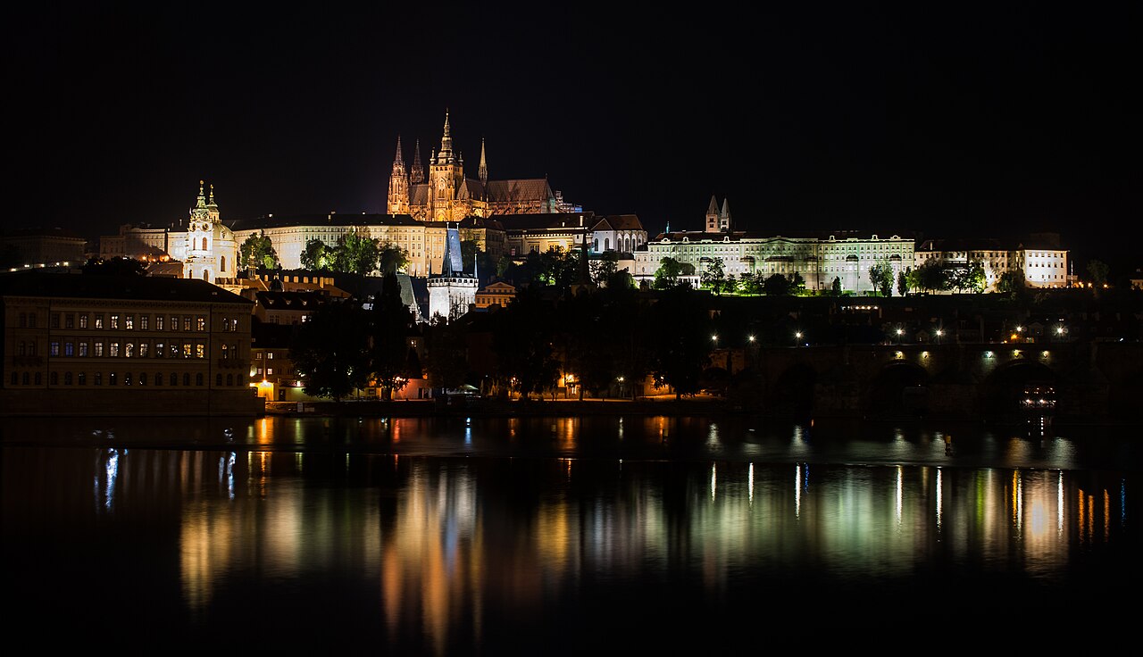 Prague Castle illuminated at night above the Vltava River.